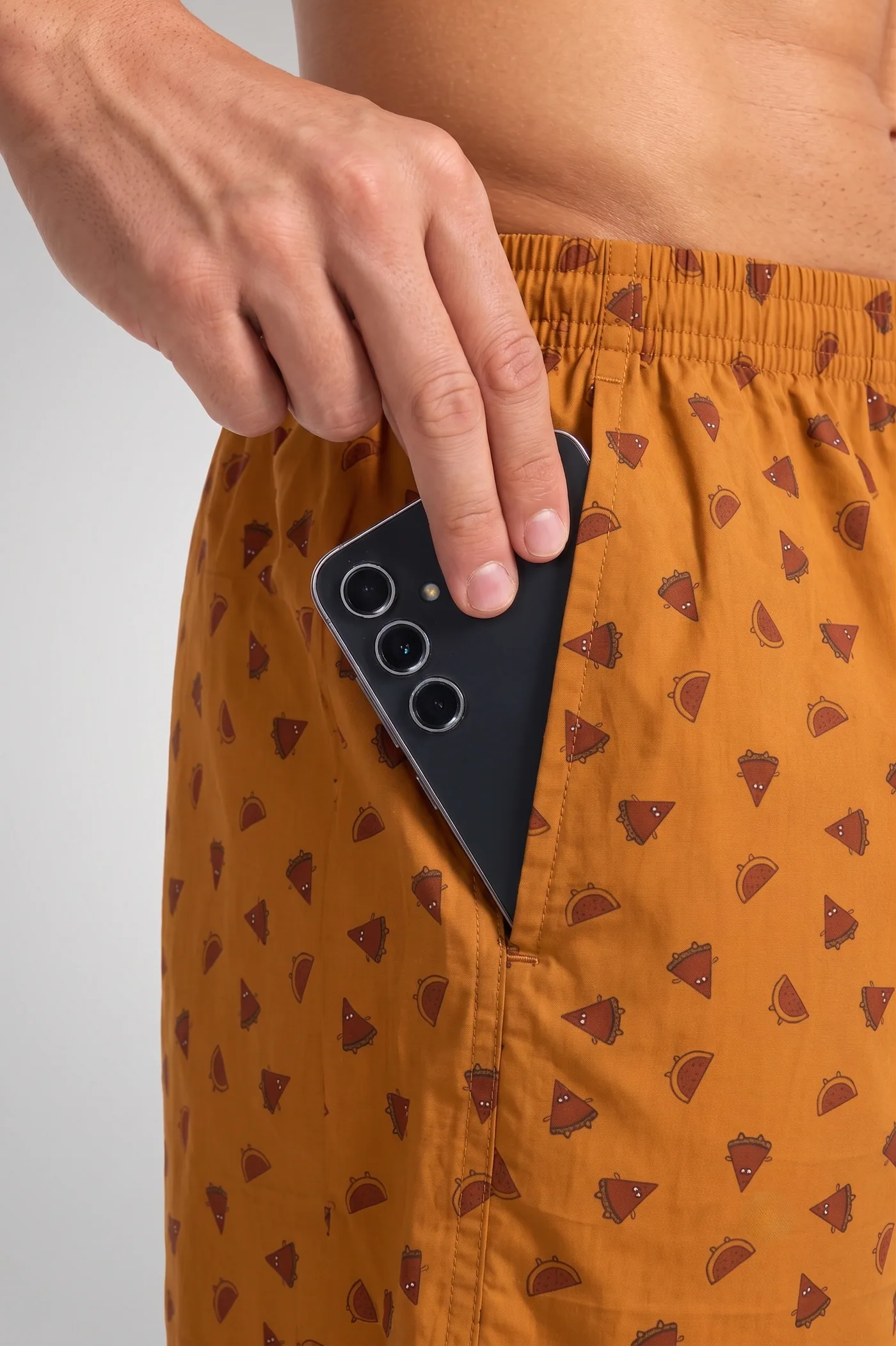 A phone sliding into the side pocket of Amber Acorn boxer shorts, showing the pocket depth