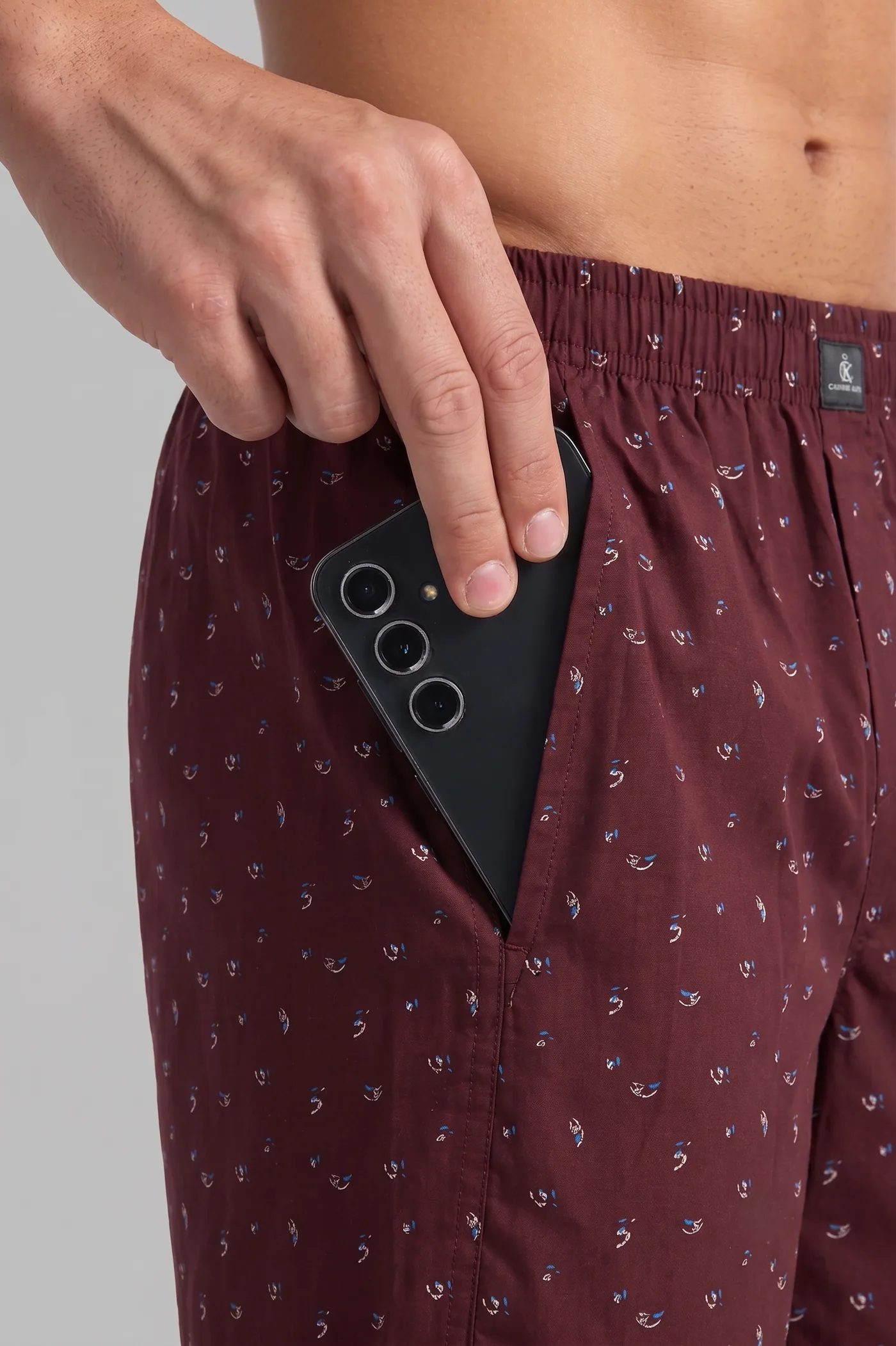 A phone sliding into the side pocket of Cabernet Petal Toss boxer shorts, showing the pocket depth